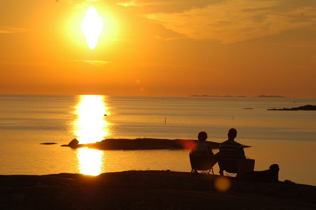 Solnedgång över havet med en familj som sitter och tittar ut på vattnet.